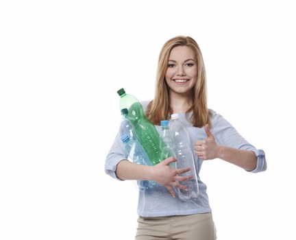 A young woman with long blonde hair and a light blue long-sleeve top is smiling and holding multiple clear plastic bottles, including a green-tinted one, against her chest with her arms crossed. She is giving a thumbs-up with her right hand. The bottles appear to be made of lightweight PET plastic with varying shapes and sizes, some with ridged surfaces and others smooth. She stands against a plain, neutral background with no visible environmental context. The overall scene conveys positivity and awareness related to recycling or waste management, aligning with rubbish removal services such as those offered by Commercial Waste Forest Hill. The image has a bright and natural lighting, emphasizing the clarity and transparency of the bottles, creating a friendly and approachable atmosphere synonymous with eco-friendly waste disposal efforts in the Forest Hill area.